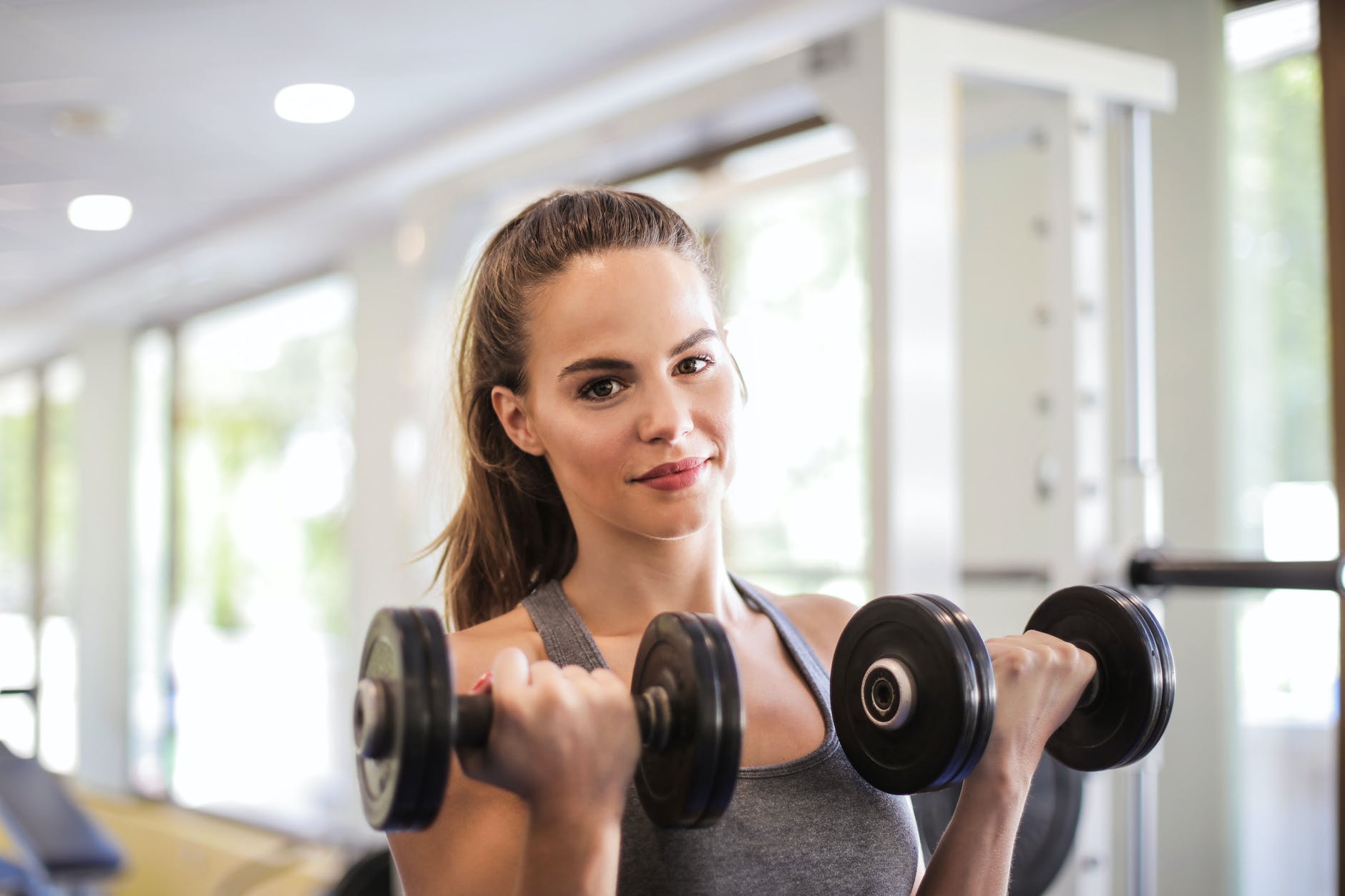 woman in gray tank top holding two black dumbbells