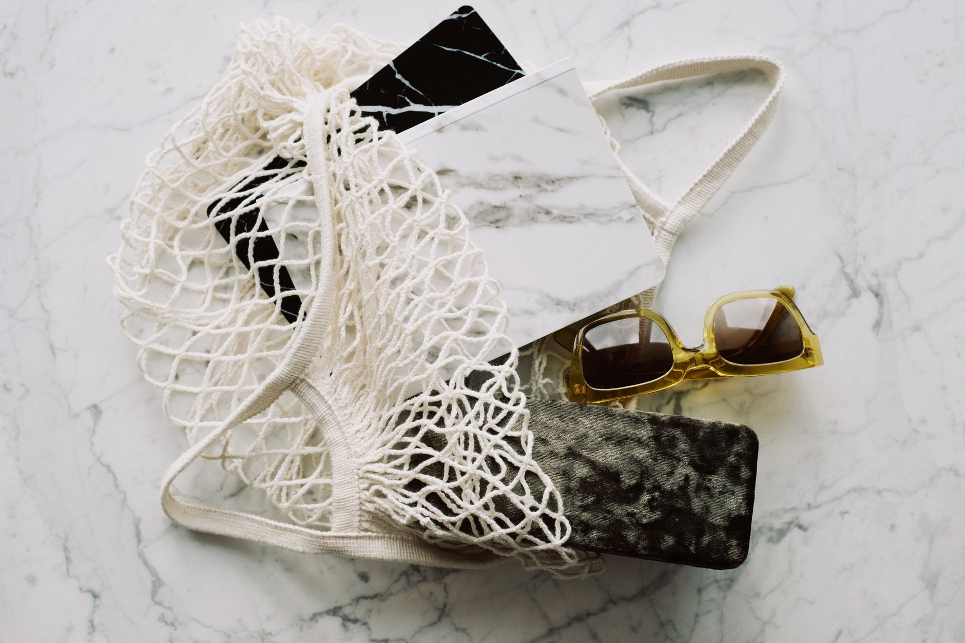 sunglasses with notepads placed in white mesh bag on marble table